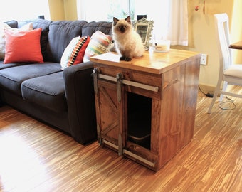 May include: A wooden cat litter box with a sliding door, finished in a dark brown stain. The box is sitting on a wooden table top with a cat sitting on the table. The cat is white with blue eyes.