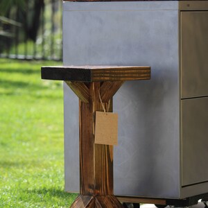 May include: A dark brown wooden stool with a triangular base and a rectangular top. The stool is next to a silver metal cabinet with wheels.