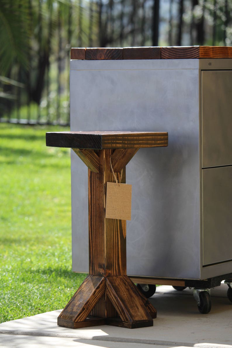 May include: A dark brown wooden stool with a triangular base and a rectangular top. The stool is next to a silver metal cabinet with wheels.