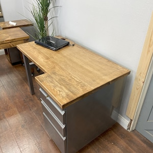 May include: A gray metal desk with a wood top and a three-drawer file cabinet. The desk has a laptop on the top and a cord plugged in.