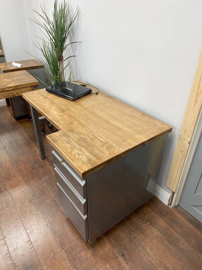 May include: A gray metal desk with a wood top and a three-drawer file cabinet. The desk has a laptop on the top and a cord plugged in.
