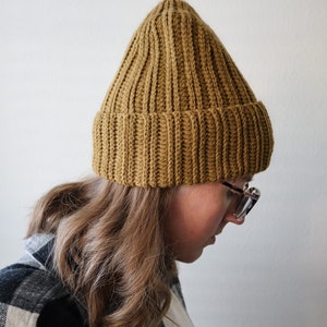 May include: A person wearing a brown knitted beanie hat and a black and white plaid shirt.