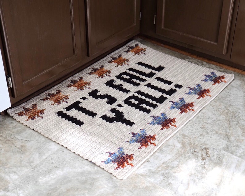 Puede incluir: Una alfombra de bienvenida de crochet blanco con texto negro que dice "It's Fall Y'all" y un borde de hojas de crochet de colores.