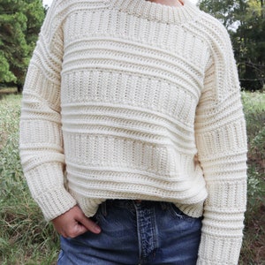 K&ouml;nnte beinhalten: Ein cremefarbener H&auml;kelpullover mit Rippenstruktur. Der Pullover hat einen runden Ausschnitt und lange &Auml;rmel.