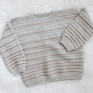 May include: A grey and brown striped knitted jumper with long sleeves and a crew neck.