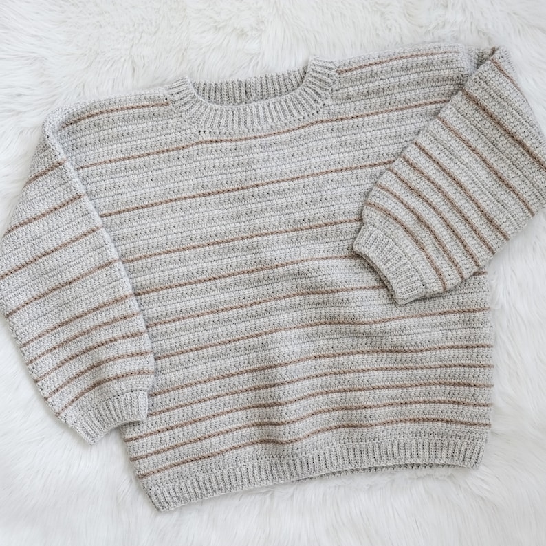 May include: A grey and brown striped knitted jumper with long sleeves and a crew neck.