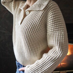 May include: A cream-colored knitted sweater with a button-up collar and a ribbed texture.