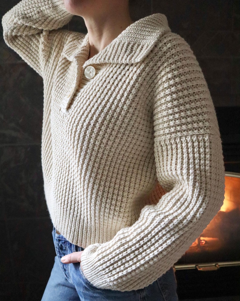 May include: A cream-colored knitted sweater with a button-up collar and a ribbed texture.