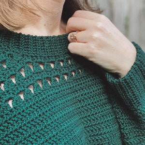 May include: A close-up of a green crocheted sweater with a delicate openwork pattern around the neckline.