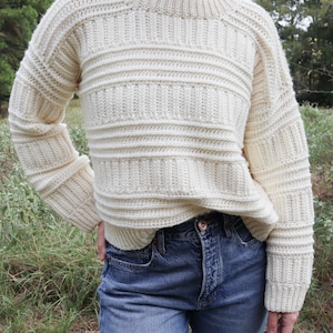 K&ouml;nnte beinhalten: Ein wei&szlig;er H&auml;kelpullover mit Rippenmuster. Der Pullover hat einen Rundhalsausschnitt und lange &Auml;rmel.