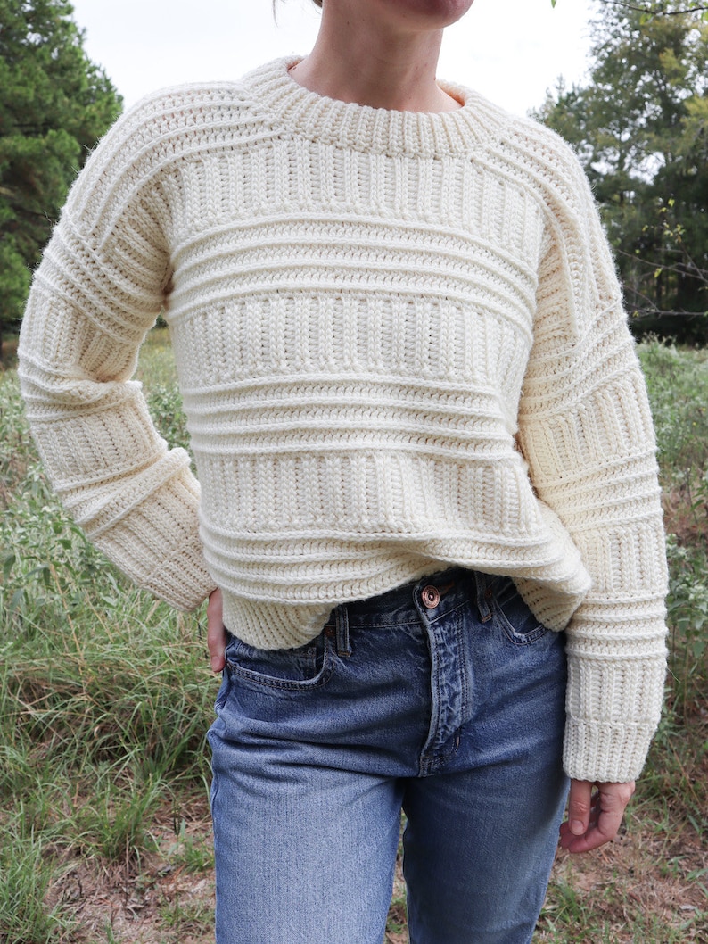 K&ouml;nnte beinhalten: Ein wei&szlig;er H&auml;kelpullover mit Rippenmuster. Der Pullover hat einen Rundhalsausschnitt und lange &Auml;rmel.