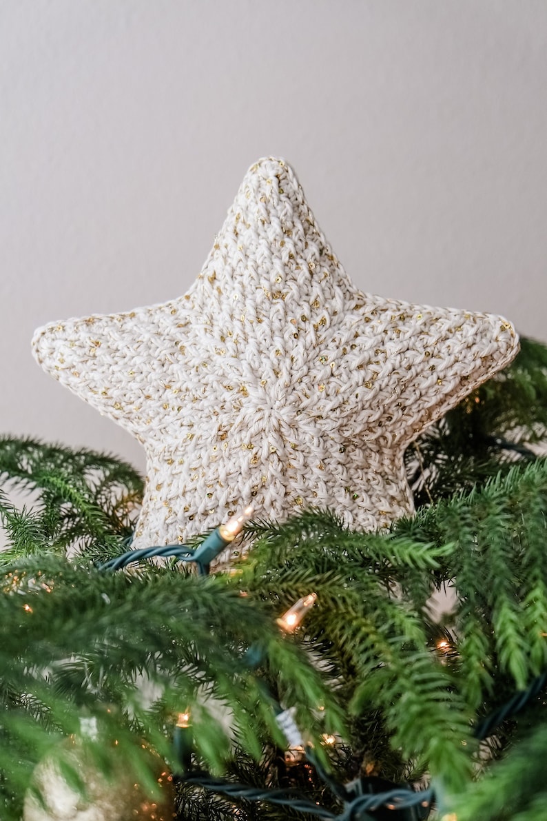 May include: A white crocheted star with gold glitter accents, used as a Christmas tree topper.