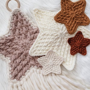 May include: A set of five crocheted stars in various shades of brown, pink, and white. The stars are hanging from a wooden ring and have long white yarn tassels.