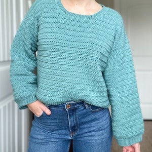 May include: A teal blue crocheted sweater with long sleeves and a round neckline.