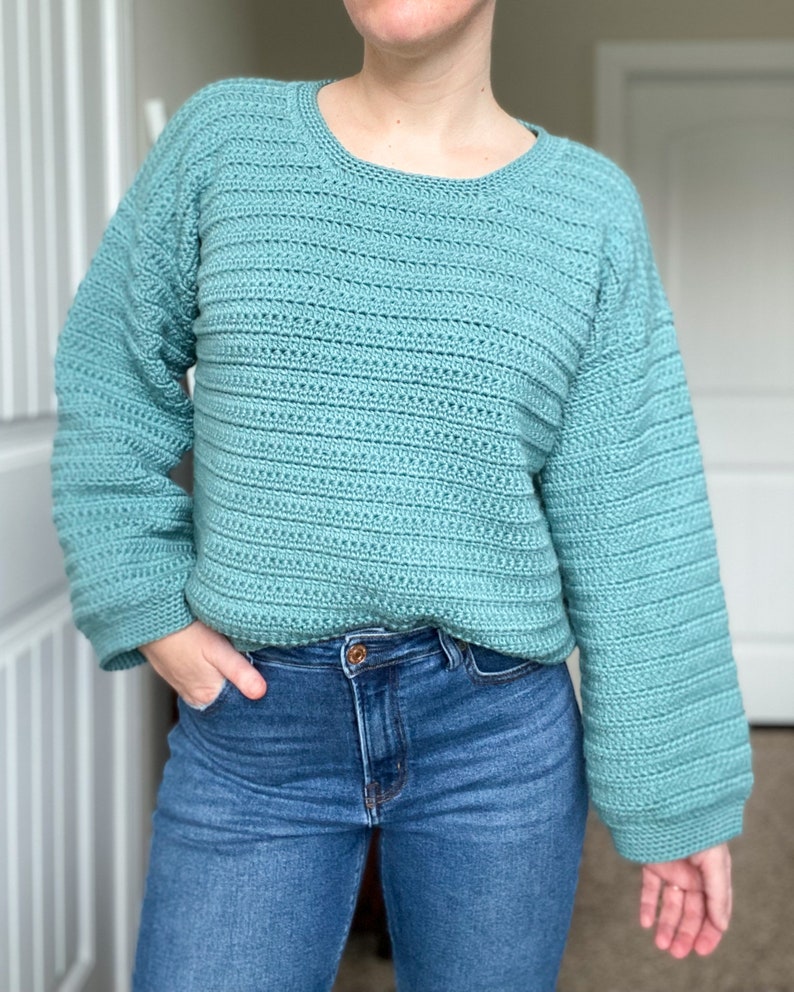 May include: A teal blue crocheted sweater with long sleeves and a round neckline.