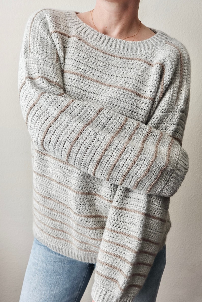 May include: A striped jumper in shades of grey and brown. The jumper has a relaxed fit and a round neckline.