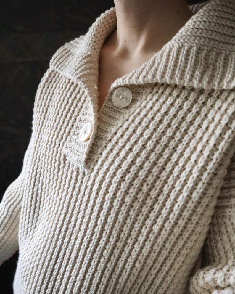 May include: A cream-colored knitted sweater with a wide collar and two button closures.