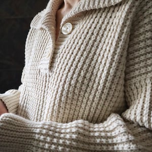 May include: A cream-colored knitted cardigan with a button closure and a ribbed texture.