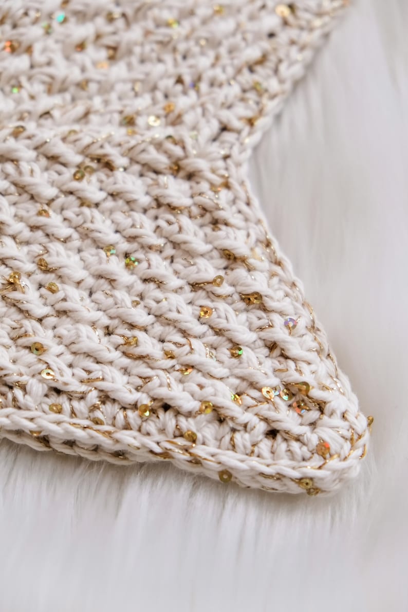 May include: Close-up of a white crocheted fabric with gold sequins. The fabric has a textured, woven look.