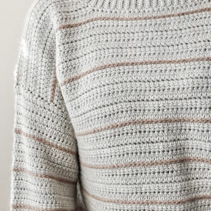 May include: A grey and brown striped crocheted jumper with long sleeves.