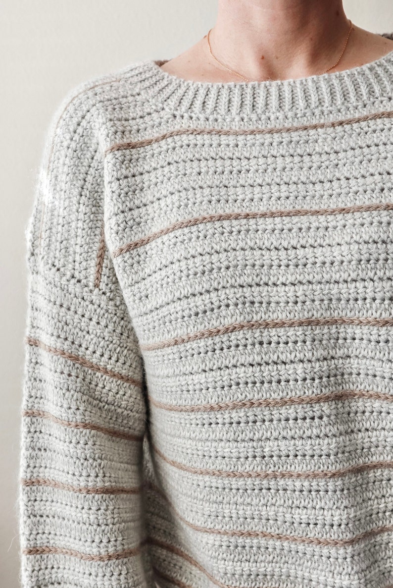 May include: A grey and brown striped crocheted jumper with long sleeves.