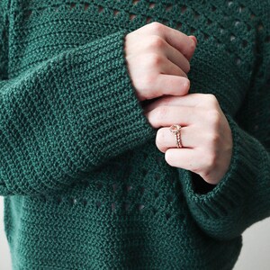 May include: A dark green crocheted sweater with a lacy pattern around the neckline and sleeves. The sweater is cropped and has a relaxed fit.