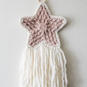 May include: A pink and white crocheted star with a white fringe hanging from a wooden ring.