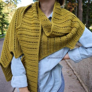 Könnte beinhalten: Senfgelber gehäkelter Schal mit strukturiertem, offen gewebtem Design. Der Schal ist über einem hellblauen Jeanshemd drapiert. Die Häkelarbeit weist horizontale Reihen offener Räume auf, was einen leichten und luftigen Look erzeugt.