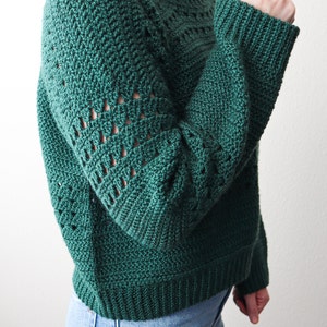 May include: A green crocheted sweater with a loose fit and a textured stitch pattern. The sweater has a round neckline and long sleeves.