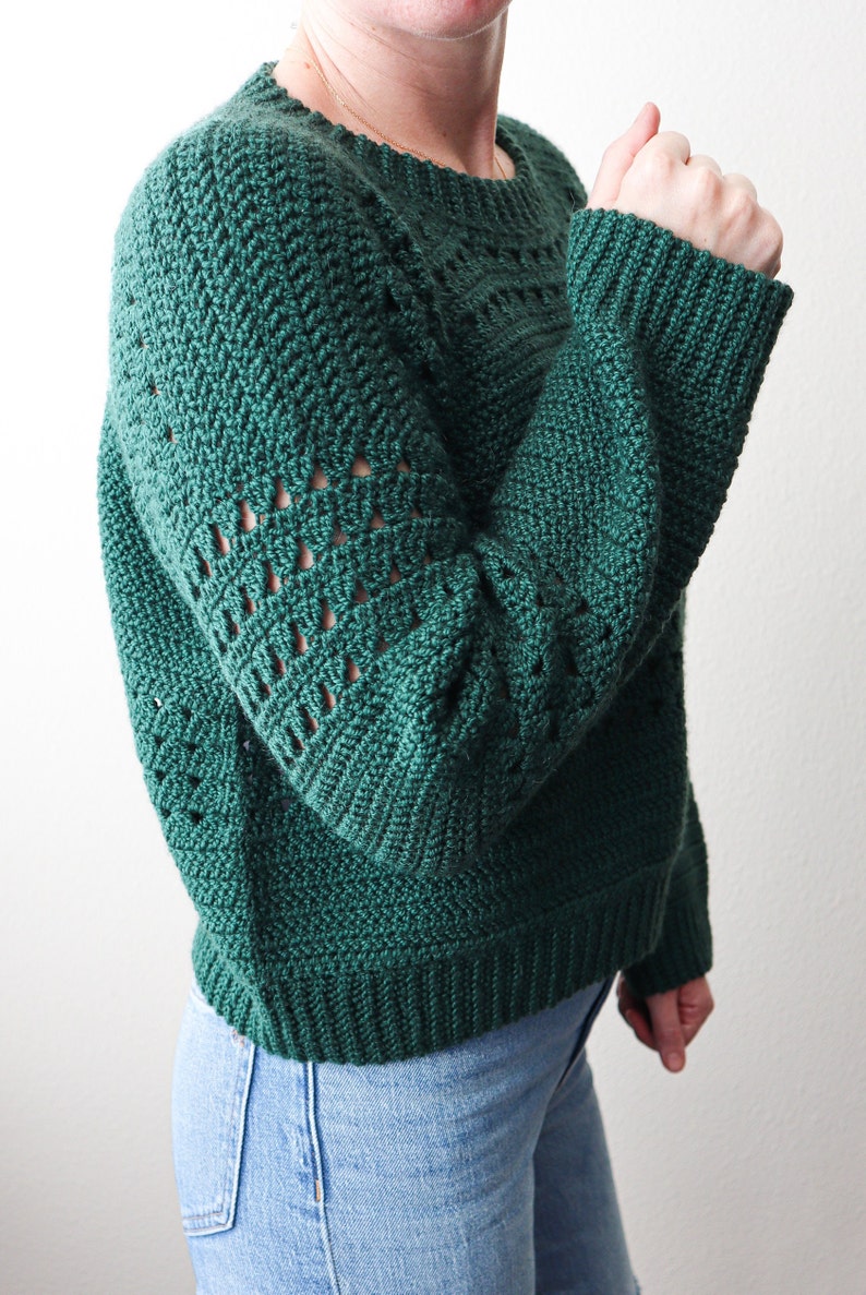 May include: A green crocheted sweater with a loose fit and a textured stitch pattern. The sweater has a round neckline and long sleeves.