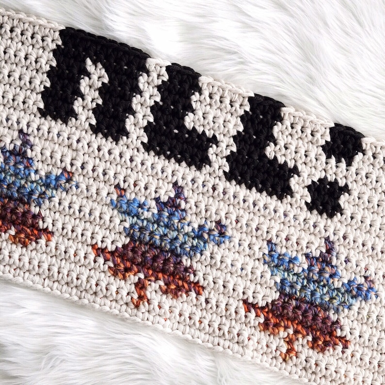 Puede incluir: Una manta de ganchillo con un patr&oacute;n geom&eacute;trico en blanco y negro en la parte superior y un patr&oacute;n multicolor en la parte inferior. La manta est&aacute; hecha con una variedad de colores, incluyendo azul, marr&oacute;n y naranja.