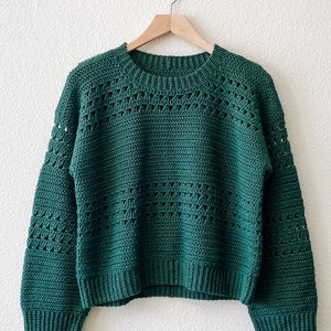 May include: A green crocheted sweater with a round neckline and long sleeves. The sweater has a loose fit and a textured pattern.