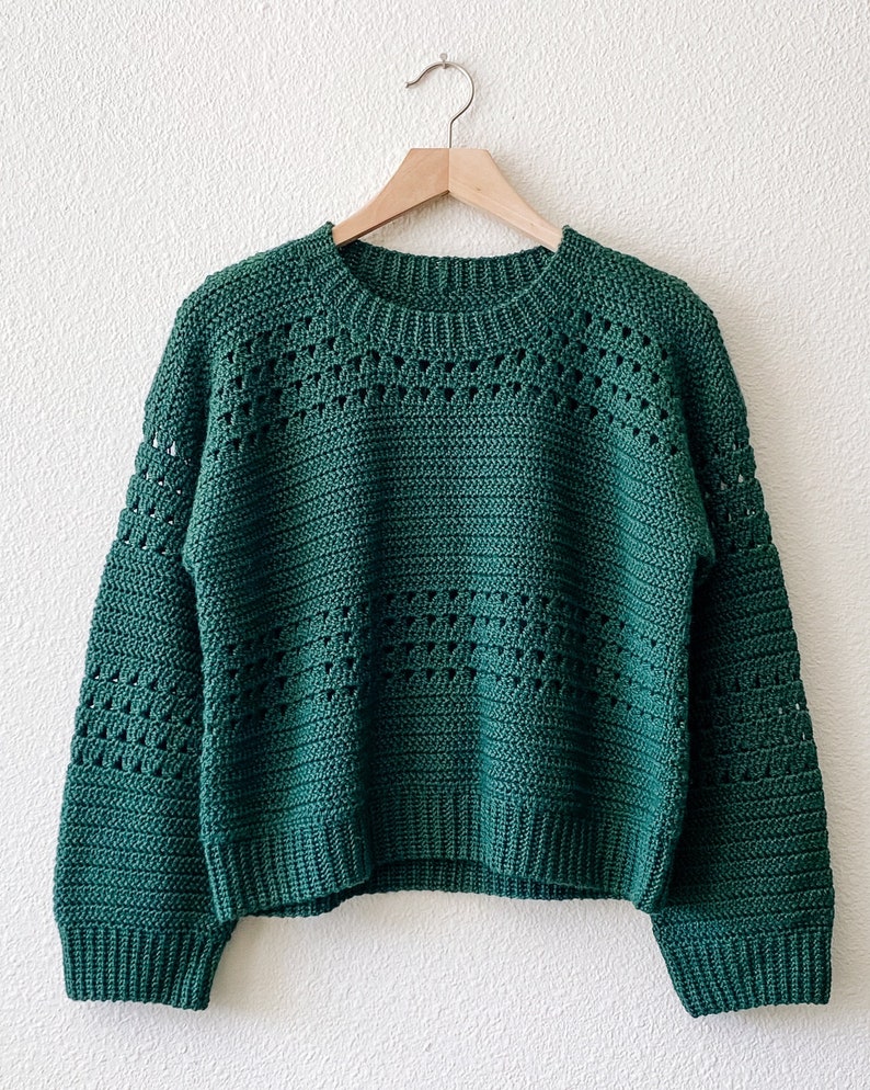 May include: A green crocheted sweater with a round neckline and long sleeves. The sweater has a loose fit and a textured pattern.
