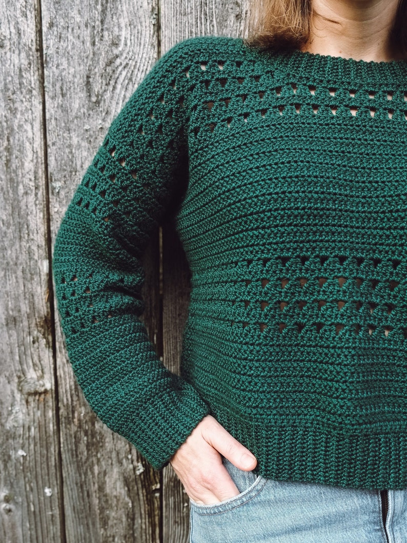 May include: A green crocheted sweater with a lacy pattern. The sweater has long sleeves and a round neckline.