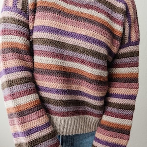 Pu&ograve; includere: Un maglione a righe lavorato a uncinetto in tonalit&agrave; di marrone, viola, rosa e beige. Il maglione ha una vestibilit&agrave; rilassata e maniche lunghe.