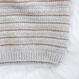 May include: A close-up of a grey and brown striped crocheted fabric. The fabric has a textured, knitted look and feel.