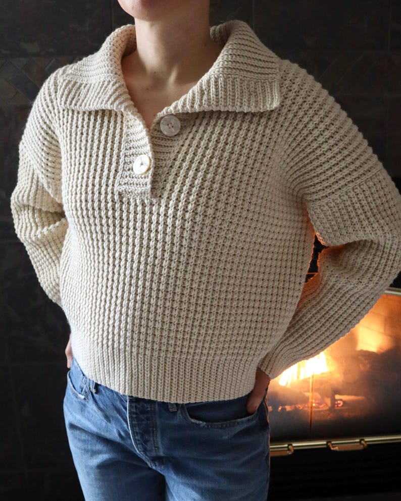 May include: A cream-colored waffle knit sweater with a button-up collar and long sleeves. The sweater is cropped and has a relaxed fit.