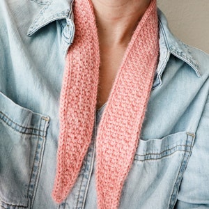 K&ouml;nnte beinhalten: Ein rosa gestrickter Schal, der um den Hals einer Person getragen wird, die ein Jeanshemd tr&auml;gt.