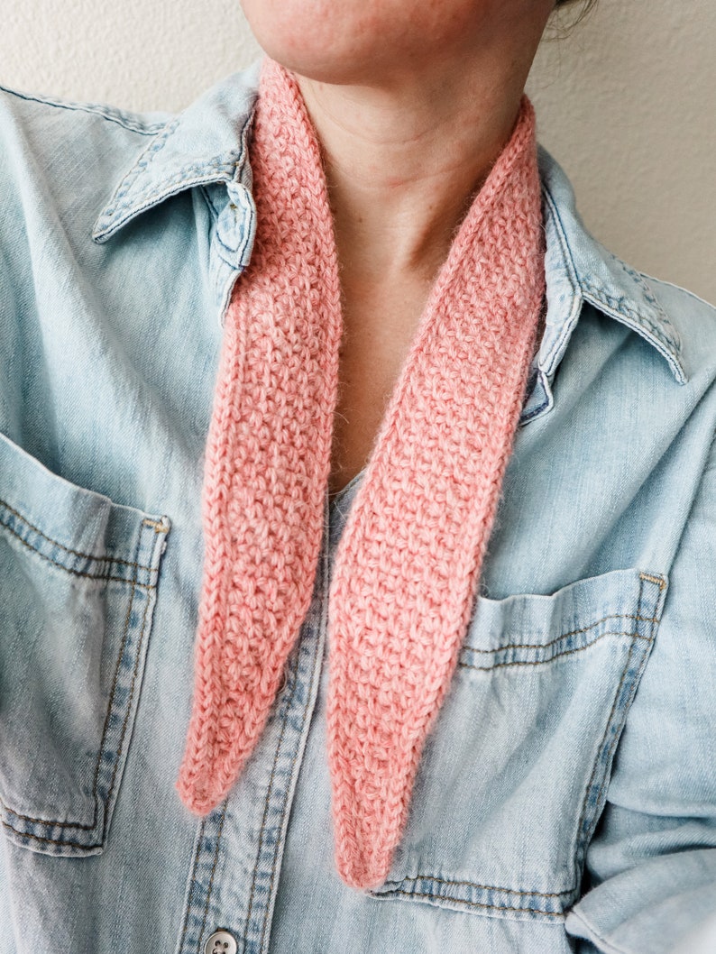 K&ouml;nnte beinhalten: Ein rosa gestrickter Schal, der um den Hals einer Person getragen wird, die ein Jeanshemd tr&auml;gt.