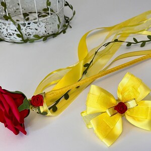 May include: A yellow wand with a red rose and green leaves at the end, a yellow bow with a red rose in the center, and yellow ribbons.