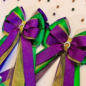 May include: Two purple, green, and gold glitter bows with silver horseshoe charms. The bows are tied with a sheer ribbon.