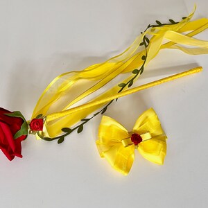 May include: A yellow wand with a red rose and green leaves at the end. A yellow bow with a red rose in the center is also included.