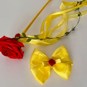 May include: A yellow satin bow with a red rose in the center, and a yellow satin ribbon with a red rose attached to a stick.