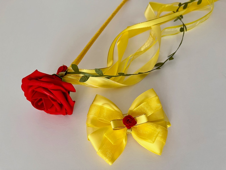 May include: A yellow satin bow with a red rose in the center, and a yellow satin ribbon with a red rose attached to a stick.