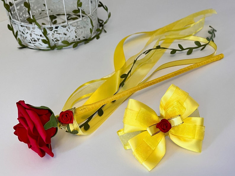 May include: A yellow wand with a red rose and green leaves at the end, a yellow bow with a red rose in the center, and yellow ribbons.
