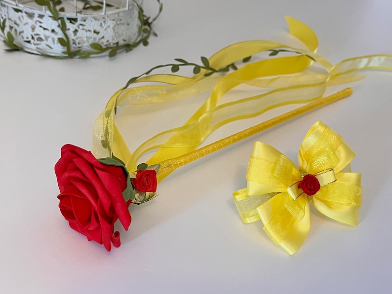 May include: A yellow wand with a red rose and a yellow bow. The wand has a yellow ribbon attached to it.