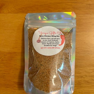 Pode incluir: Um saco de fecho hermético prateado cheio de uma mistura de especiarias castanhas. O rótulo diz "Unique Gifts Etc. Spicy Chicken Wing Mix. Delicious flavor will add spice to your food! Perfected mixture of Cayenne, Garlic, Onion, Paprika and more! Excellent for wings! NET WT. 2(OZ) DRY SPICES"