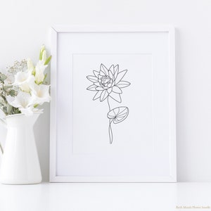 May include: A black and white line drawing of a water lily flower with a single leaf. The drawing is framed and displayed on a white wall.