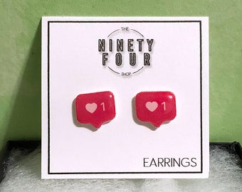 May include: A pair of red heart shaped earrings with a white heart and the number "1" inside. The earrings are displayed on a white card with the text "THE NINETY FOUR SHOP" and "EARRINGS".