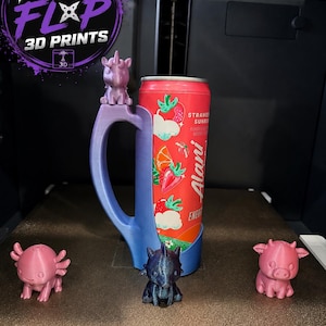 May include: A 3D-printed blue gradient can holder featuring a unicorn figure on the handle, holding a red Alani Nu Strawberry Sunrise energy drink can. Three small 3D-printed animal figurines in pink and dark blue are positioned in front.